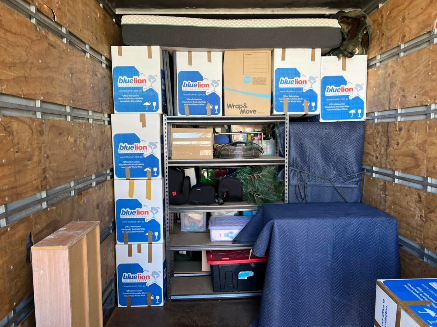 Interior of a moving truck packed with boxes, a shelf unit, and furniture wrapped in blue cloth. — Gantic Removals Ipswich in Ipswich, QLD