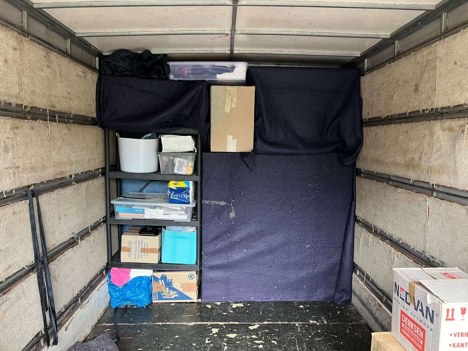 Interior of a moving truck with shelving unit and boxes of various sizes. Blue moving blanket hangs on the right wall. — Gantic Removals Ipswich in Ipswich, QLD