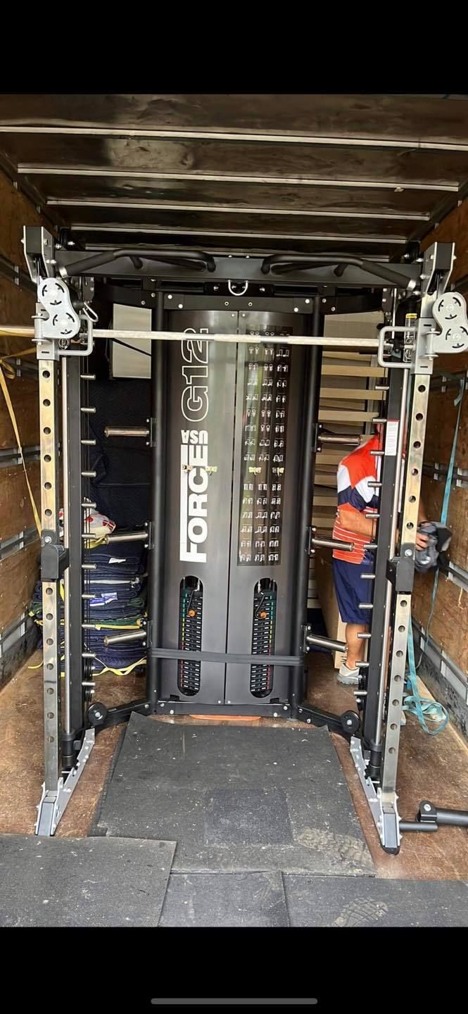 A weightlifting machine is loaded inside a truck by a person in an orange shirt.  — Gantic Removals Ipswich in Ipswich, QLD