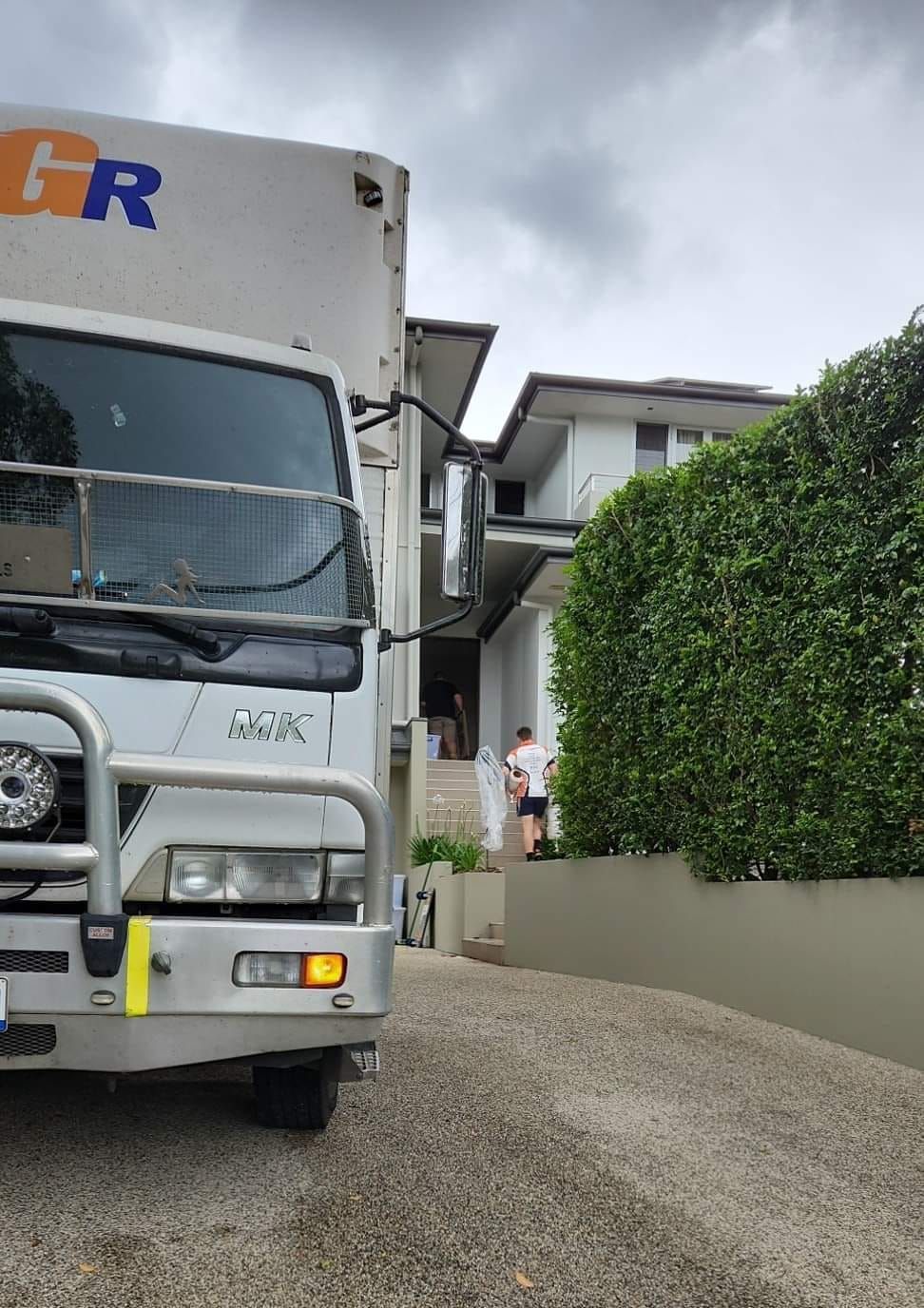 Moving truck parked in front of a white house with people carrying items up stairs. — Gantic Removals Ipswich in Ipswich, QLD