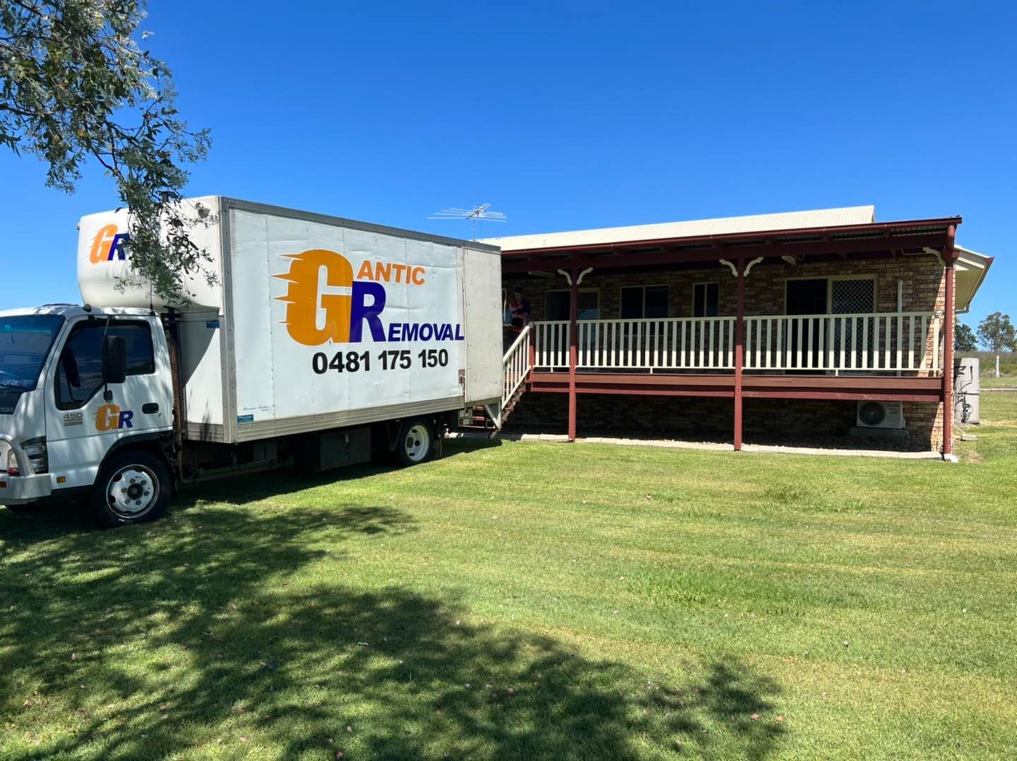 Moving truck parked next to a house with a porch, on green grass. The truck has