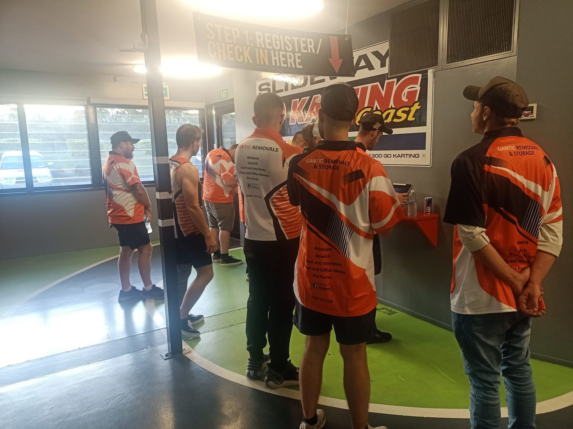 Group of people in orange and white shirts inside a room, possibly at an event, with banners on the wall — Gantic Removals Ipswich in Ipswich, QLD