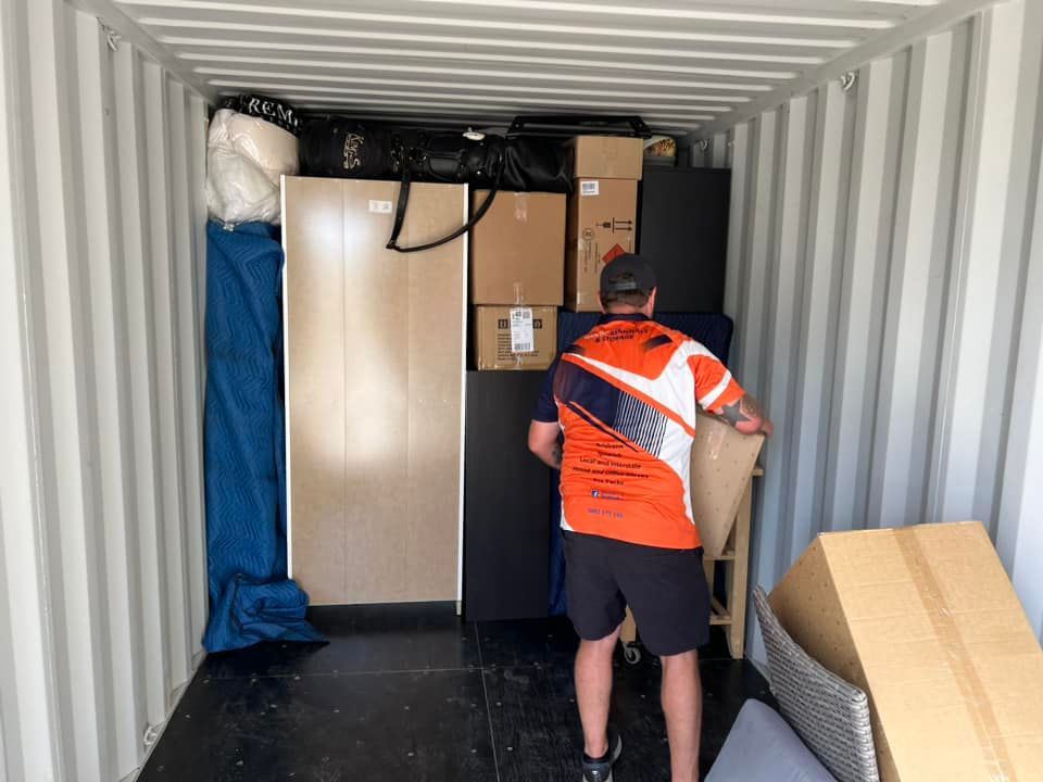 A person loading packed boxes and furniture into a storage container. Inside, boxes, and a person loading furniture. — Gantic Removals Ipswich in Ipswich, QLD