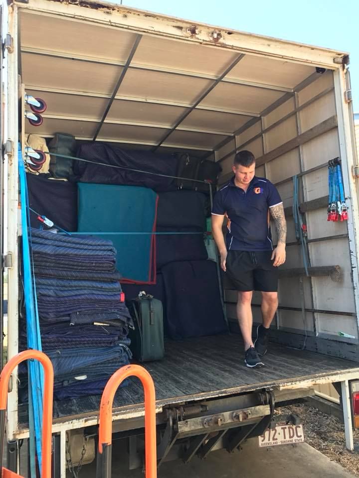 Man exiting the back of a moving truck filled with furniture wrapped in blue pads.— Gantic Removals Ipswich in Ipswich, QLD