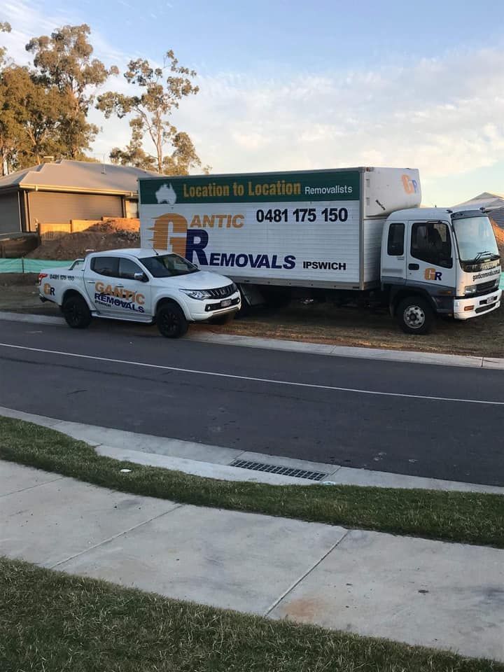 White moving truck and white pickup truck parked on the side of a road in front of a house — Gantic Removals Ipswich in Ipswich, QLD