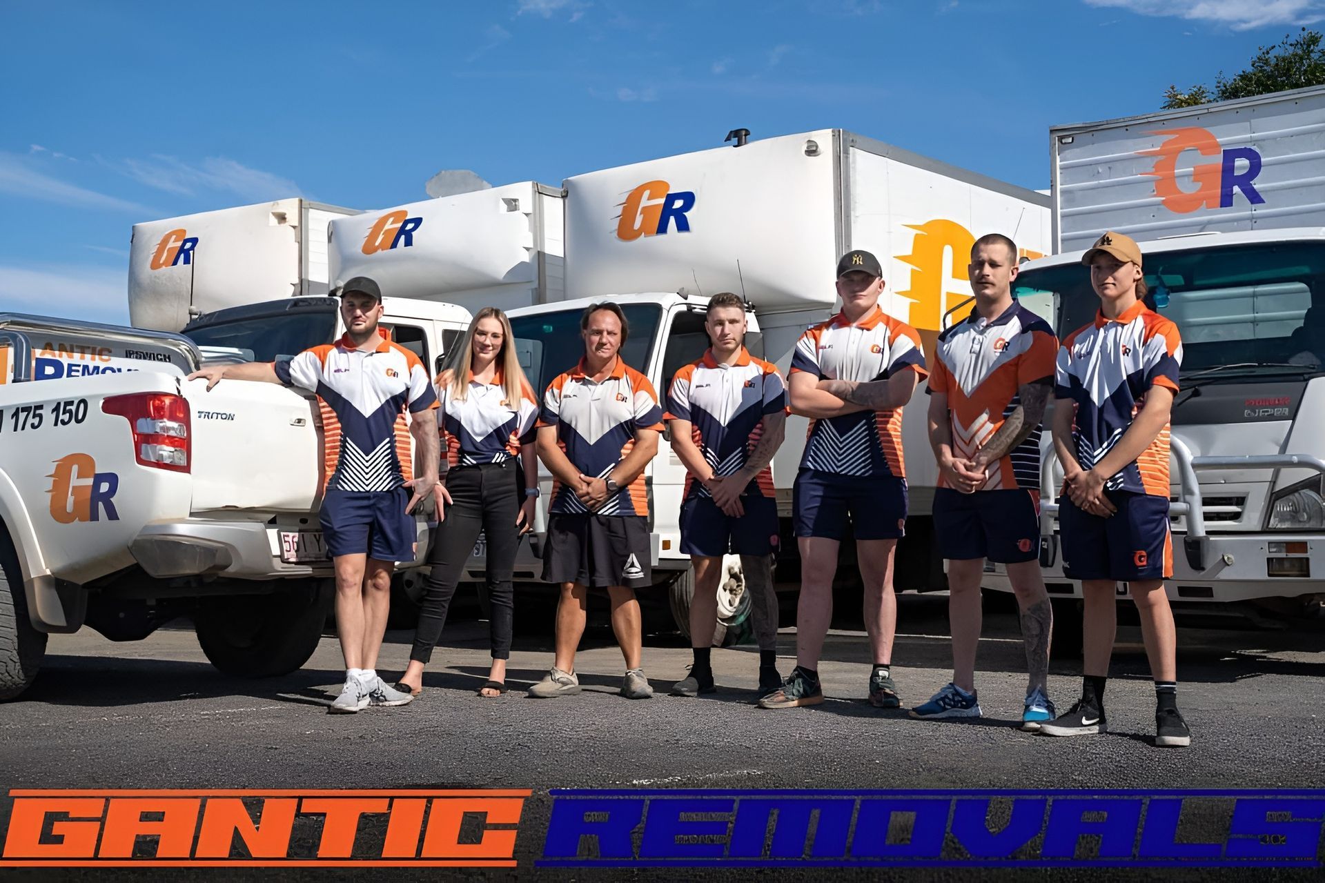 A team of people in uniforms stand in front of removal trucks with 