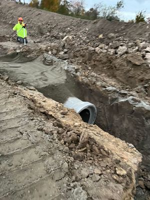 A man is standing in the dirt next to a pipe.