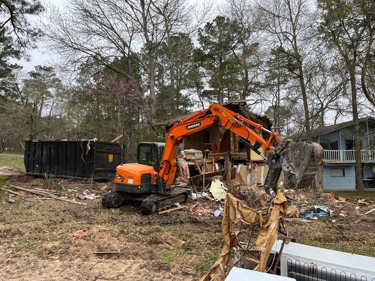 An excavator is demolishing a house in a field.