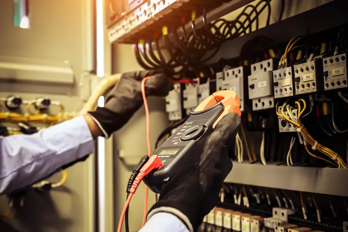 An electrician is working on an electrical panel with a multimeter.