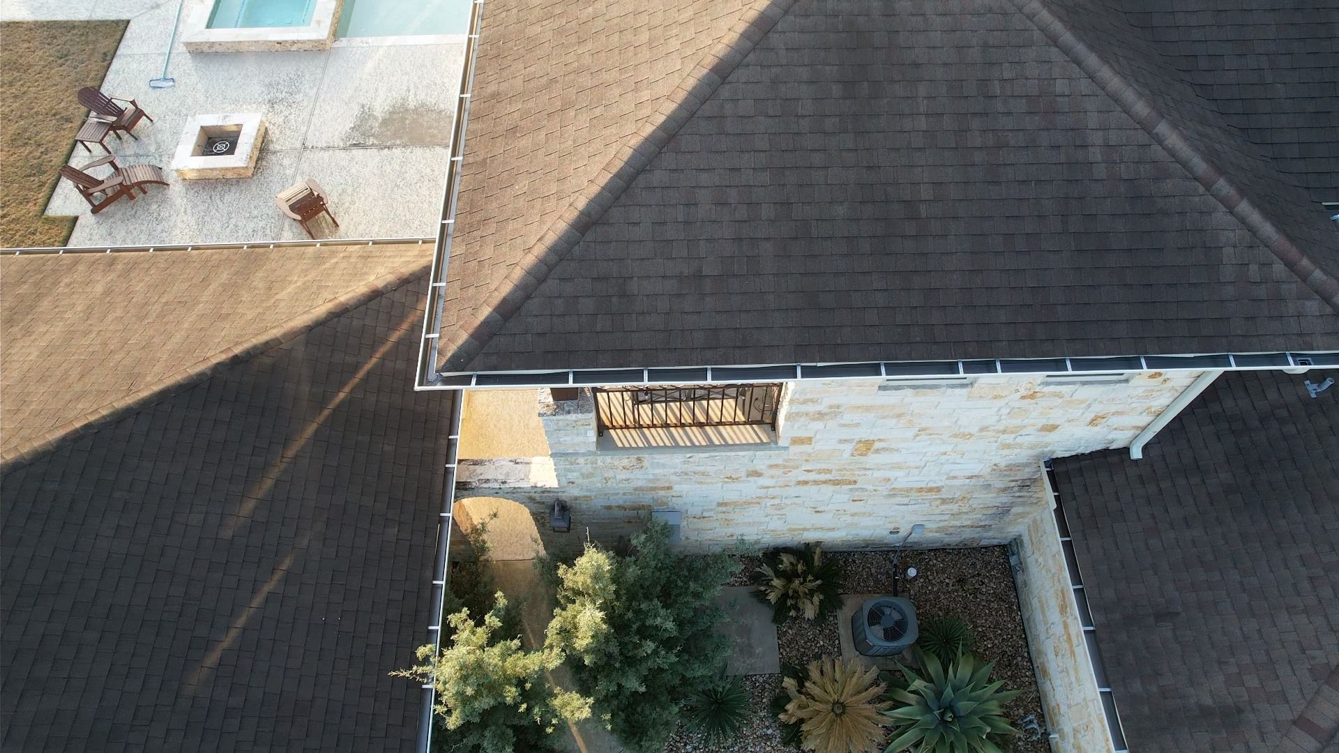 Overhead view of a house with a dark roof, stone walls, and a patio with a pool.