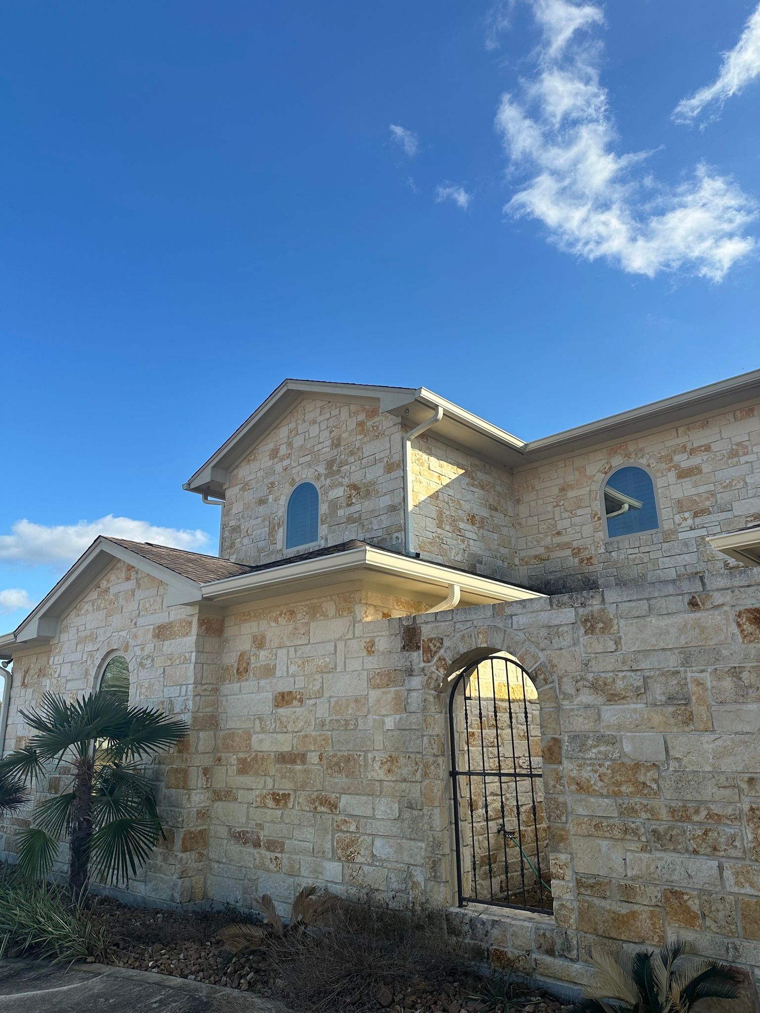 Stone house with arched windows and a wooden gate, under a blue sky with clouds.