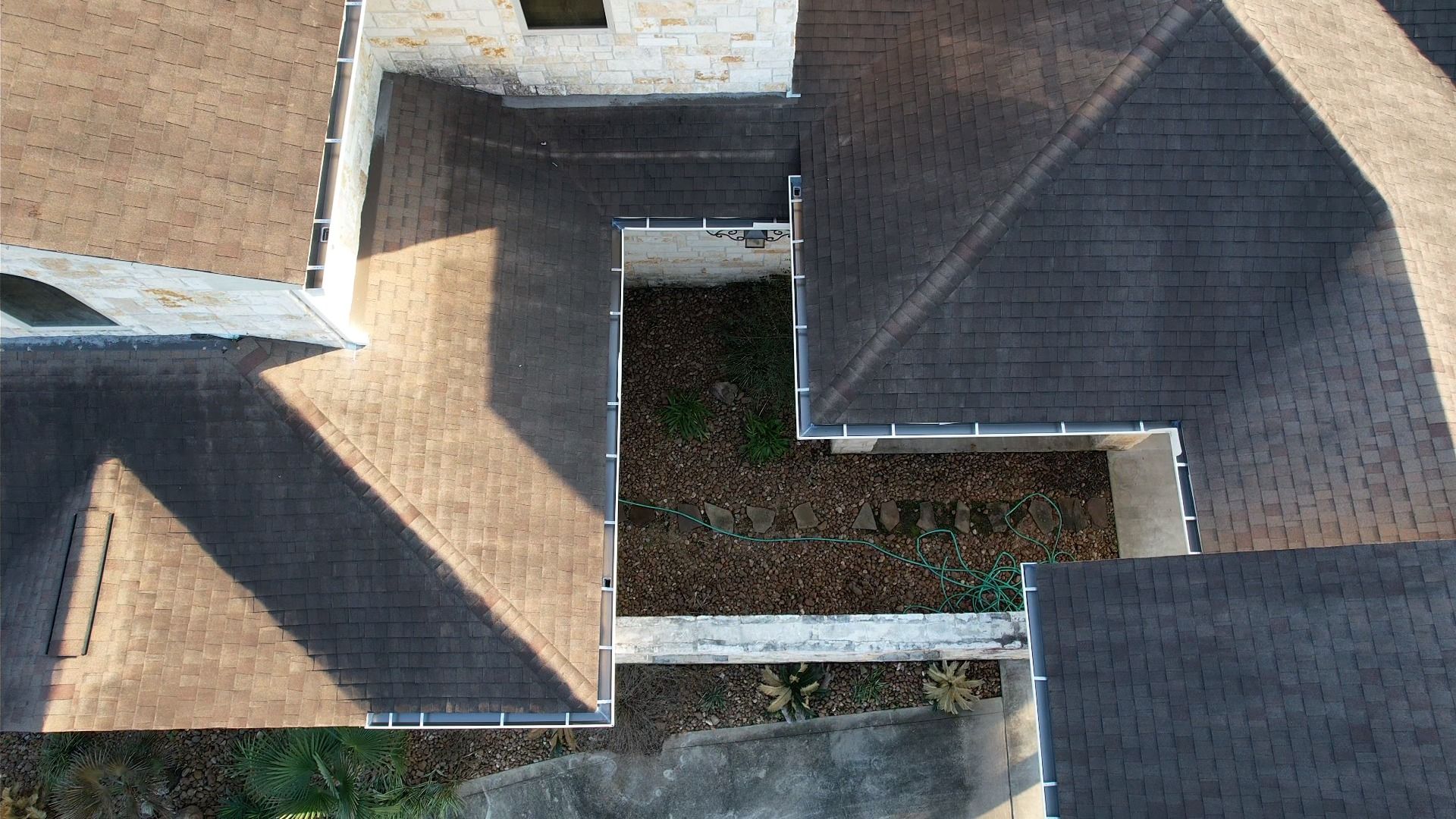 Overhead view of a building with brown and gray shingle roofs, and a courtyard filled with leaves.