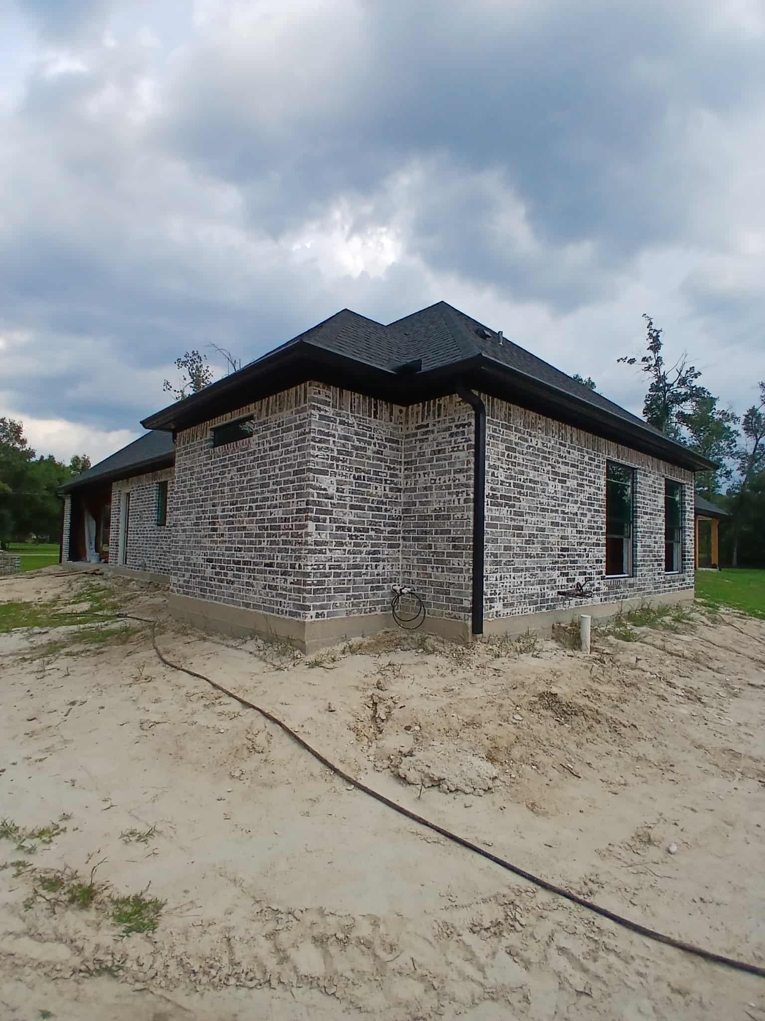 House under construction with brick facade and dark roof against a cloudy sky.