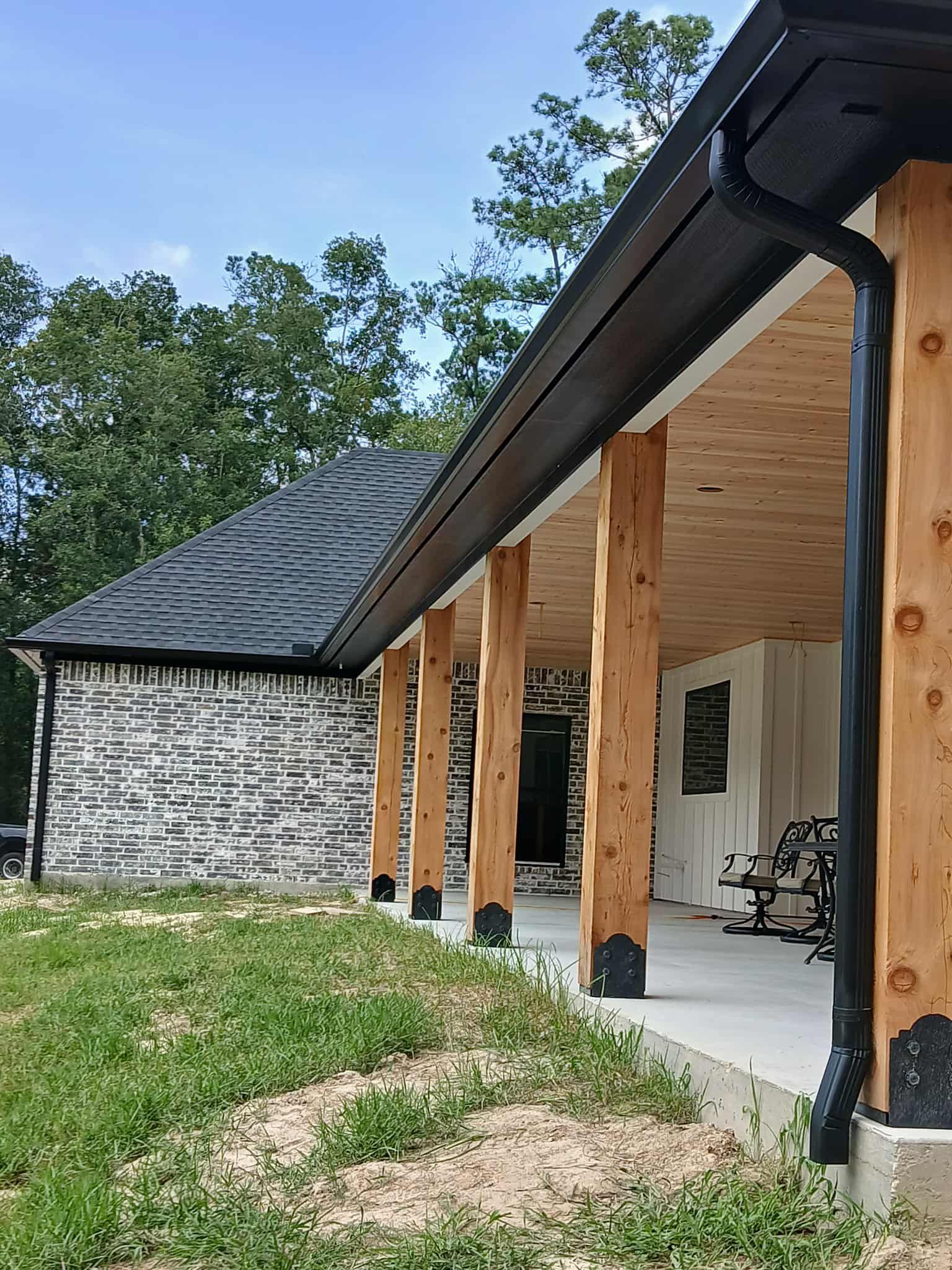 Wooden porch with black guttering, stone wall building, and a gray roof on a sunny day.