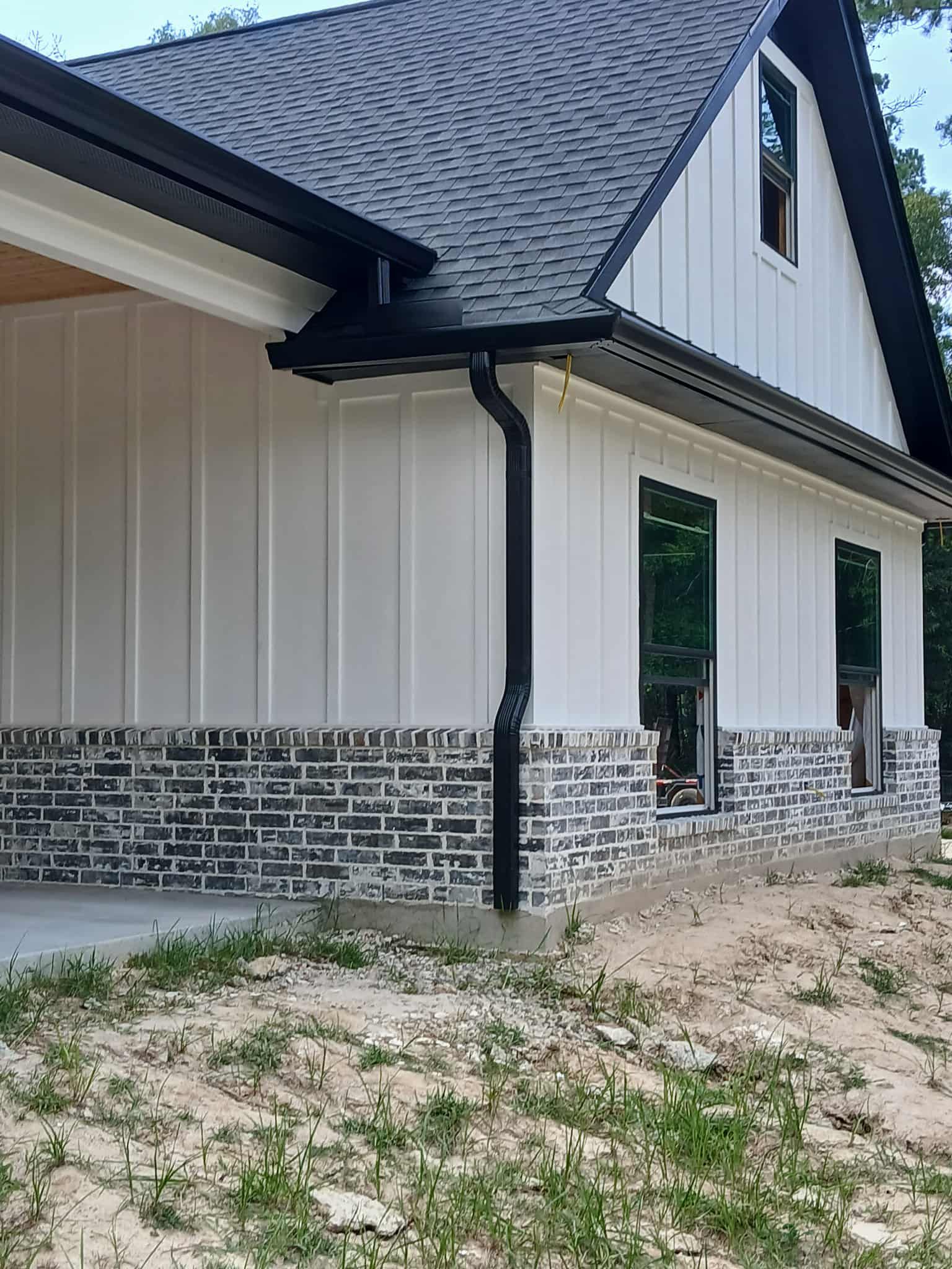 White house with black trim, brick base, and dark gray roof.