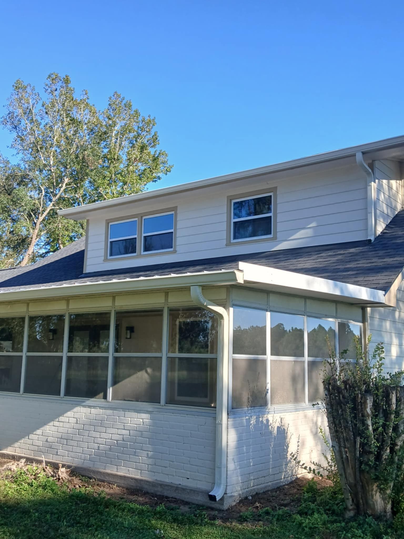 Two-story house with screened porch, gray roof, white siding, and blue sky.