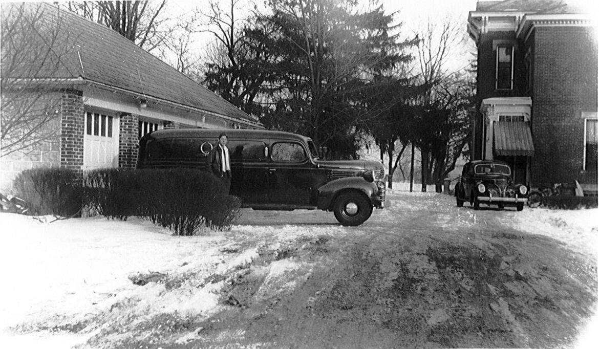 A black and white photo of a car parked in front of a house