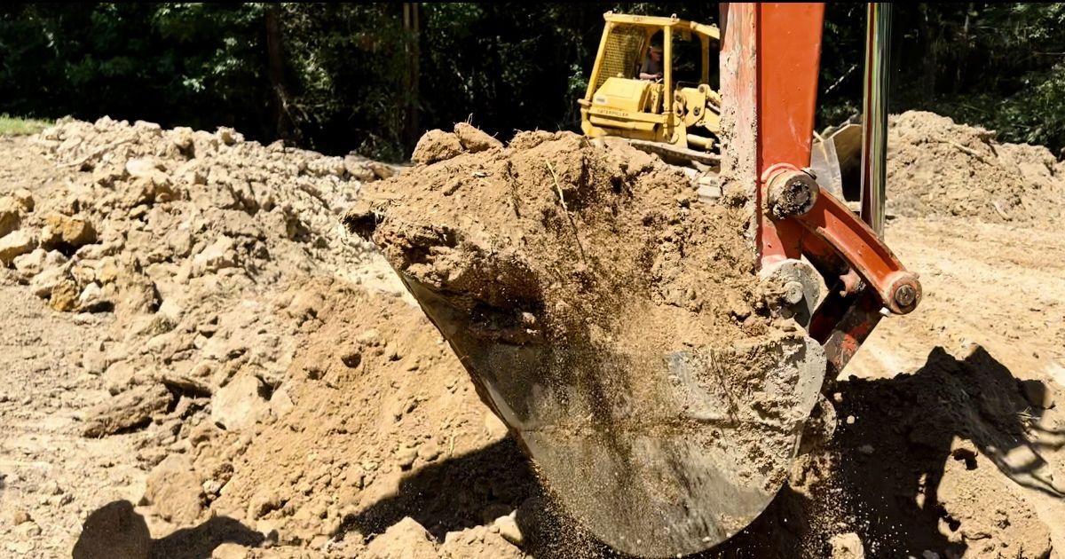 Excavator bucket digging into a sandy dirt pile at a construction site