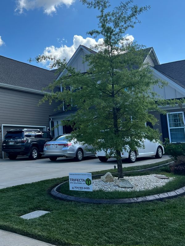 Residential driveway with two parked cars, a small tree, and a lawn sign in front of townhouses.