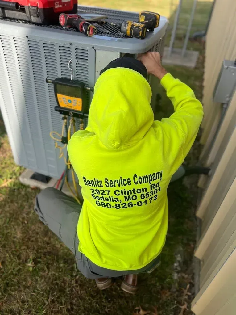 HVAC technician in a yellow hoodie services an air conditioner unit.