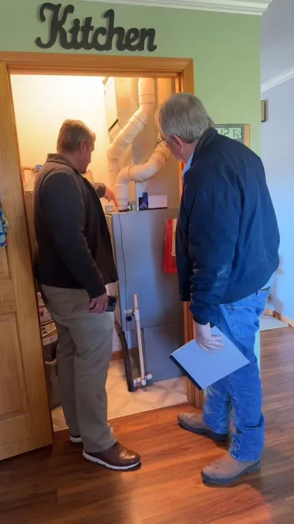 Two men examining a furnace in a small room, one pointing.