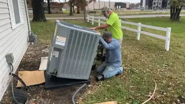 Two workers install an air conditioning unit outside a house.