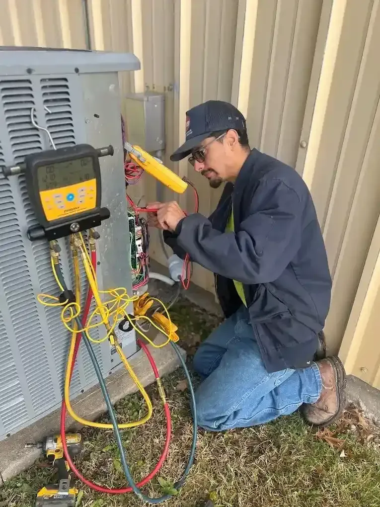 HVAC technician kneels near outdoor unit, using a multimeter on electrical components.