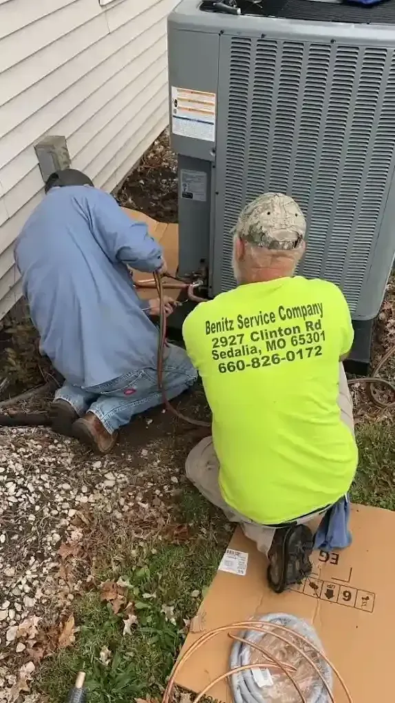 Two people installing an air conditioning unit outside a house.