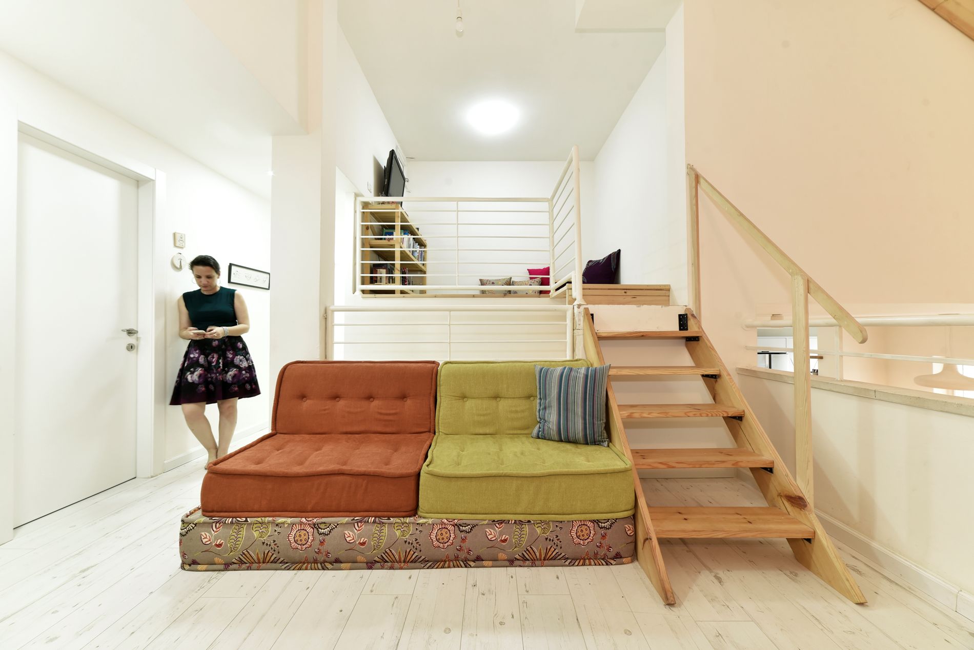 אישה עומדת בסלון ליד ספה ומדרגות.