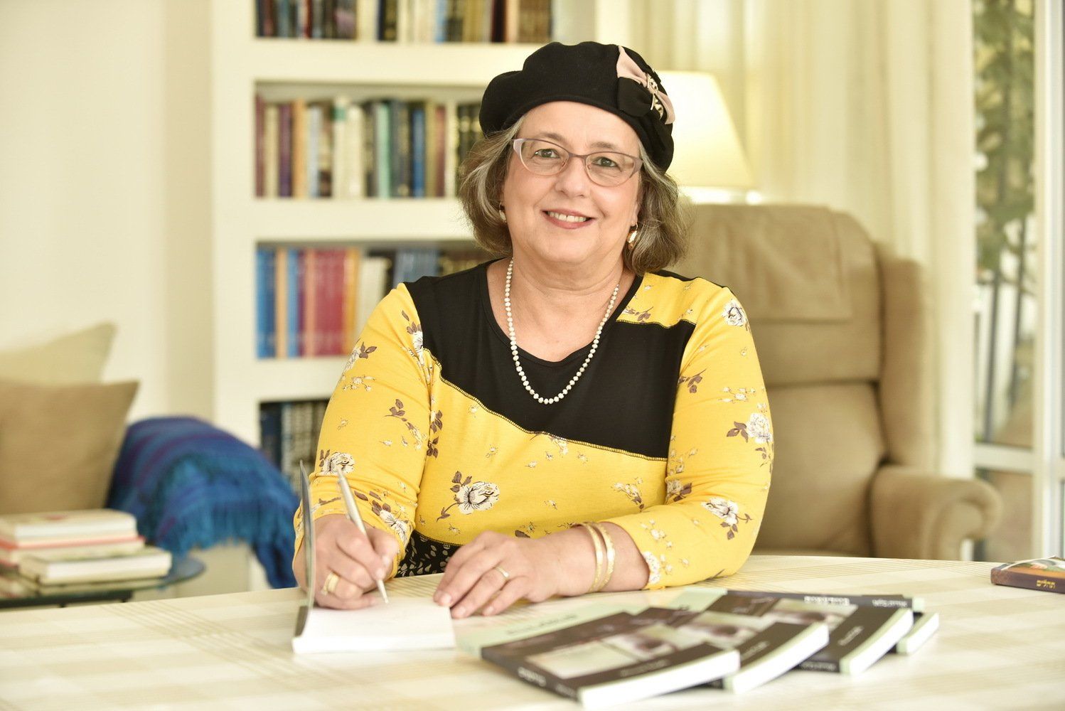 אישה יושבת ליד שולחן וכותבת במחברת.