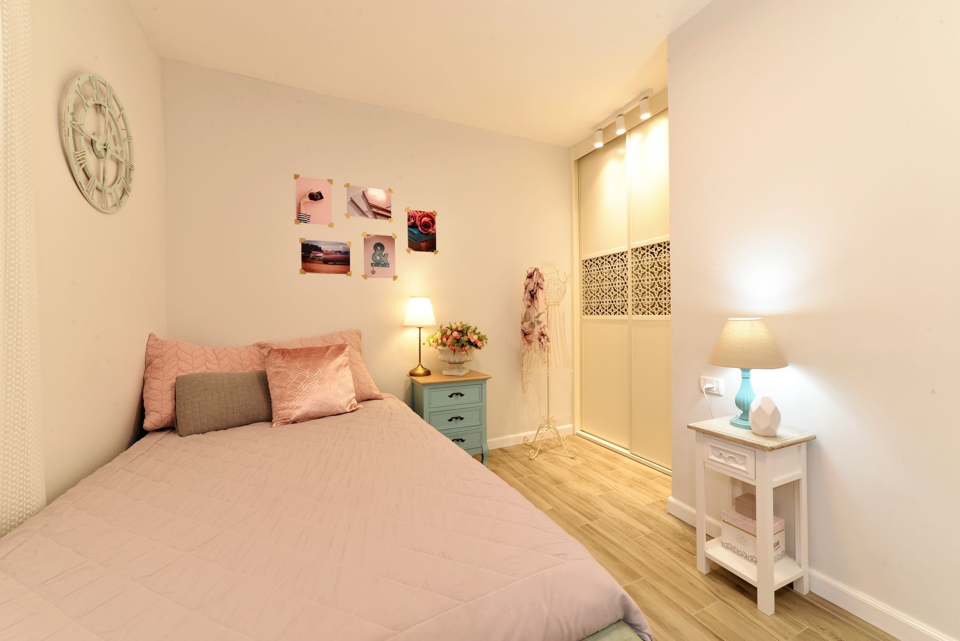 חדר שינה עם מיטה, שידת לילה, מנורה ושעון על הקיר.