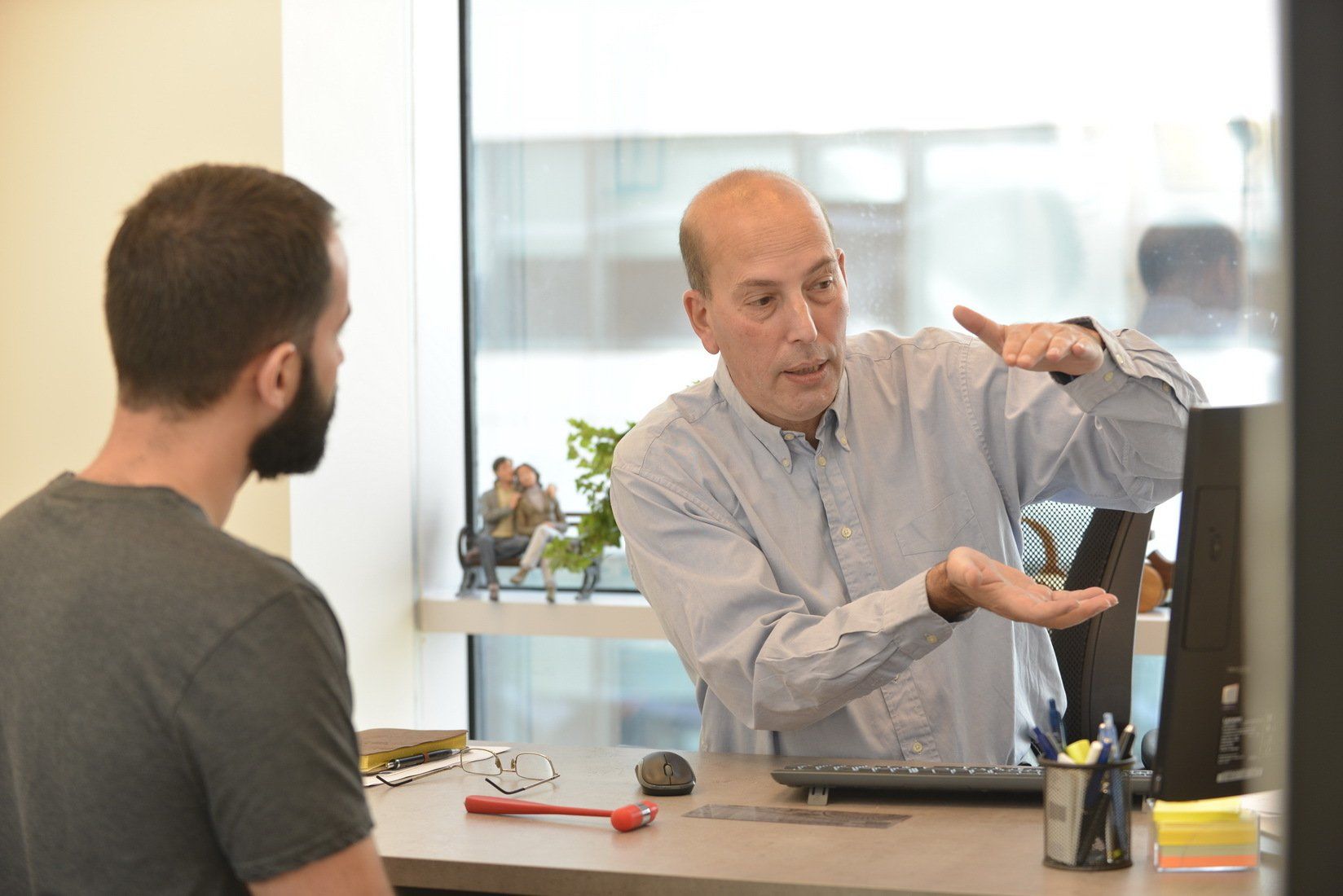 גבר יושב ליד שולחן ומדבר עם גבר אחר.