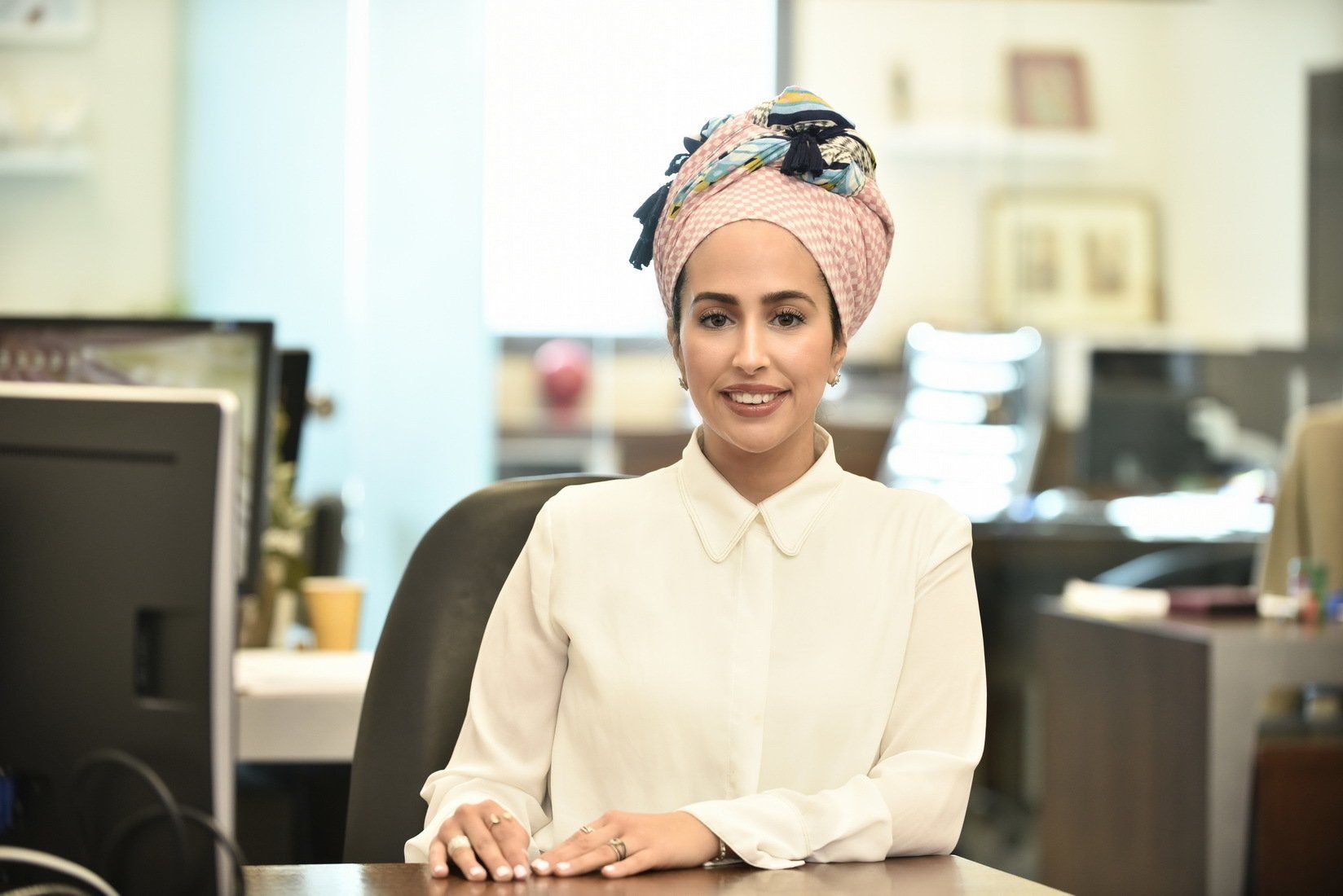 אישה חובשת טורבן יושבת ליד שולחן כתיבה מול מחשב.