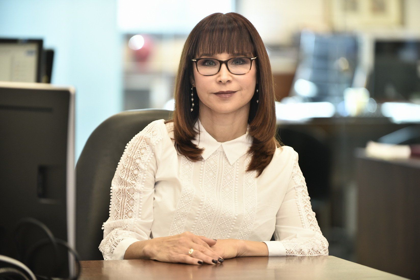 אישה מרכיבה משקפיים יושבת ליד שולחן כתיבה מול מחשב.