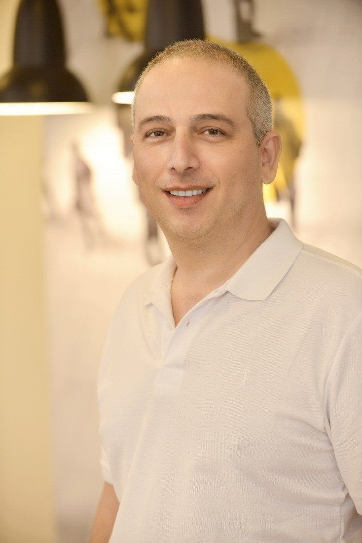 גבר בחולצה לבנה מחייך למצלמה.