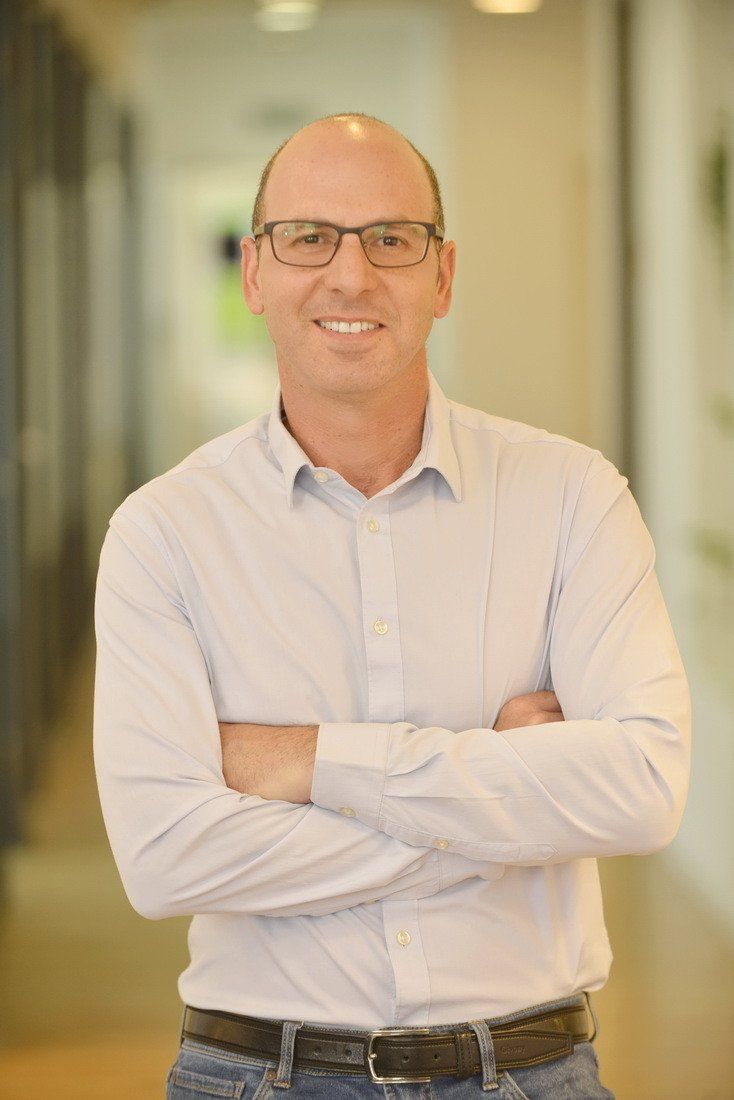 גבר מרכיב משקפיים וחולצה לבנה עומד בזרועותיו שלובות.