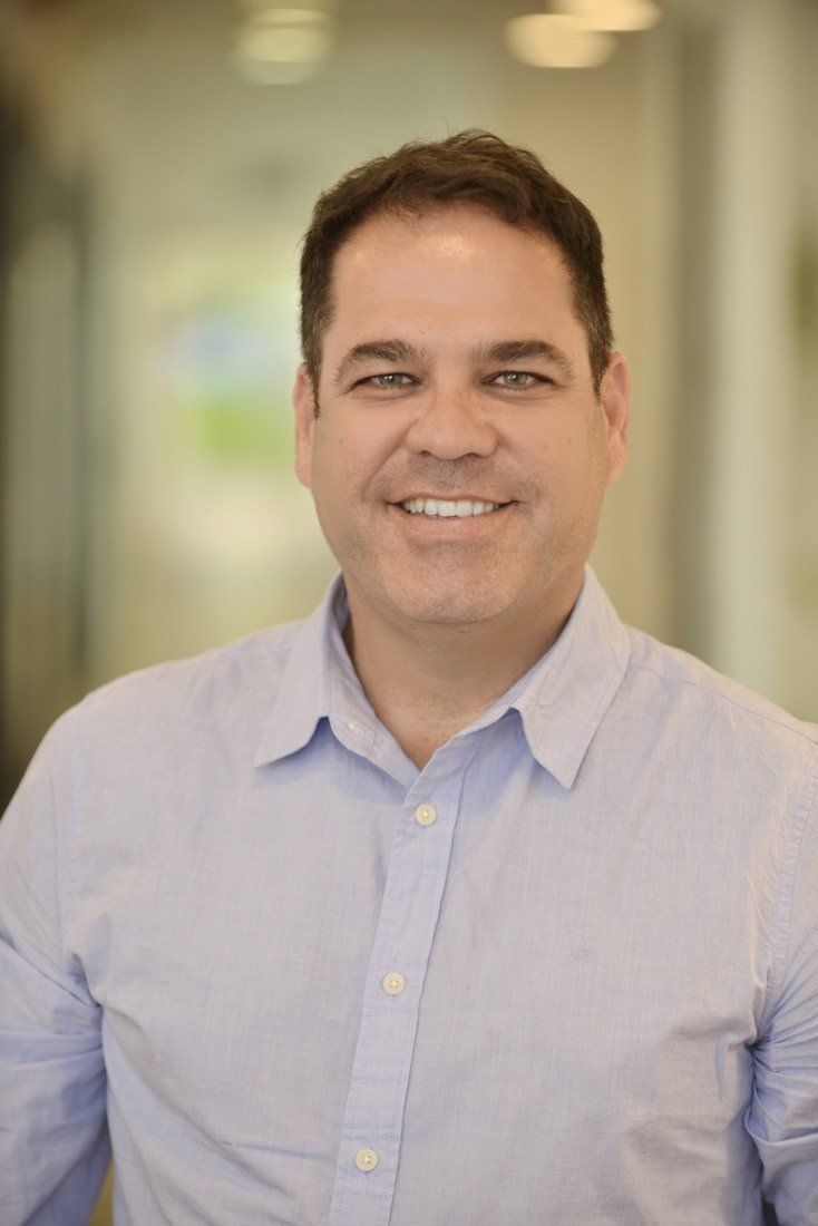 גבר בחולצה כחולה מחייך למצלמה.