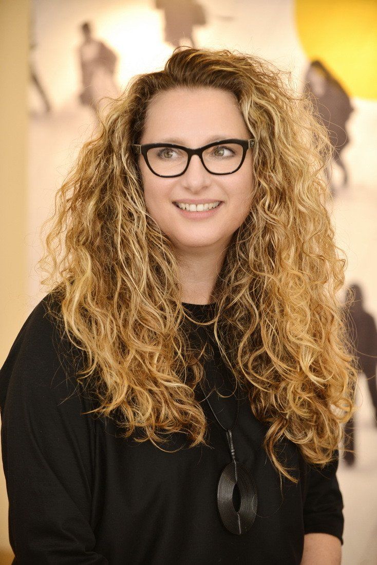 אישה עם שיער מתולתל עם משקפיים וחולצה שחורה מחייכת.