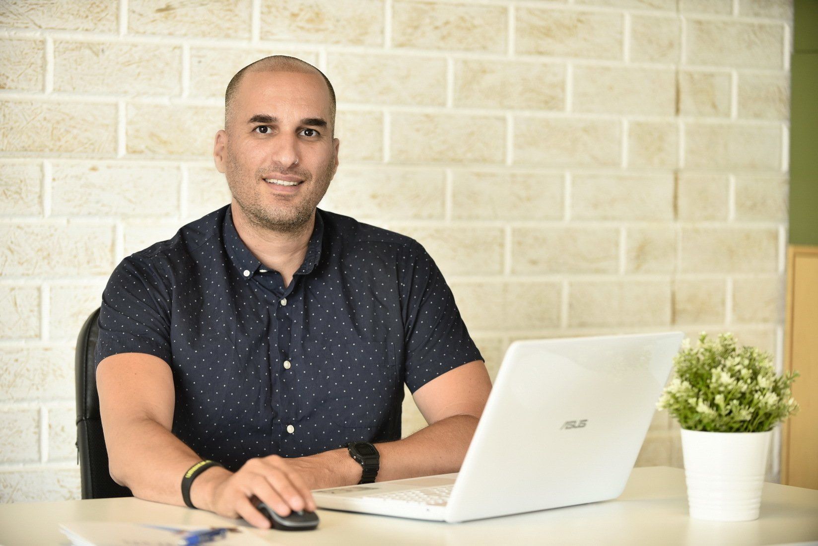 גבר יושב ליד שולחן עבודה עם מחשב נייד ועכבר.