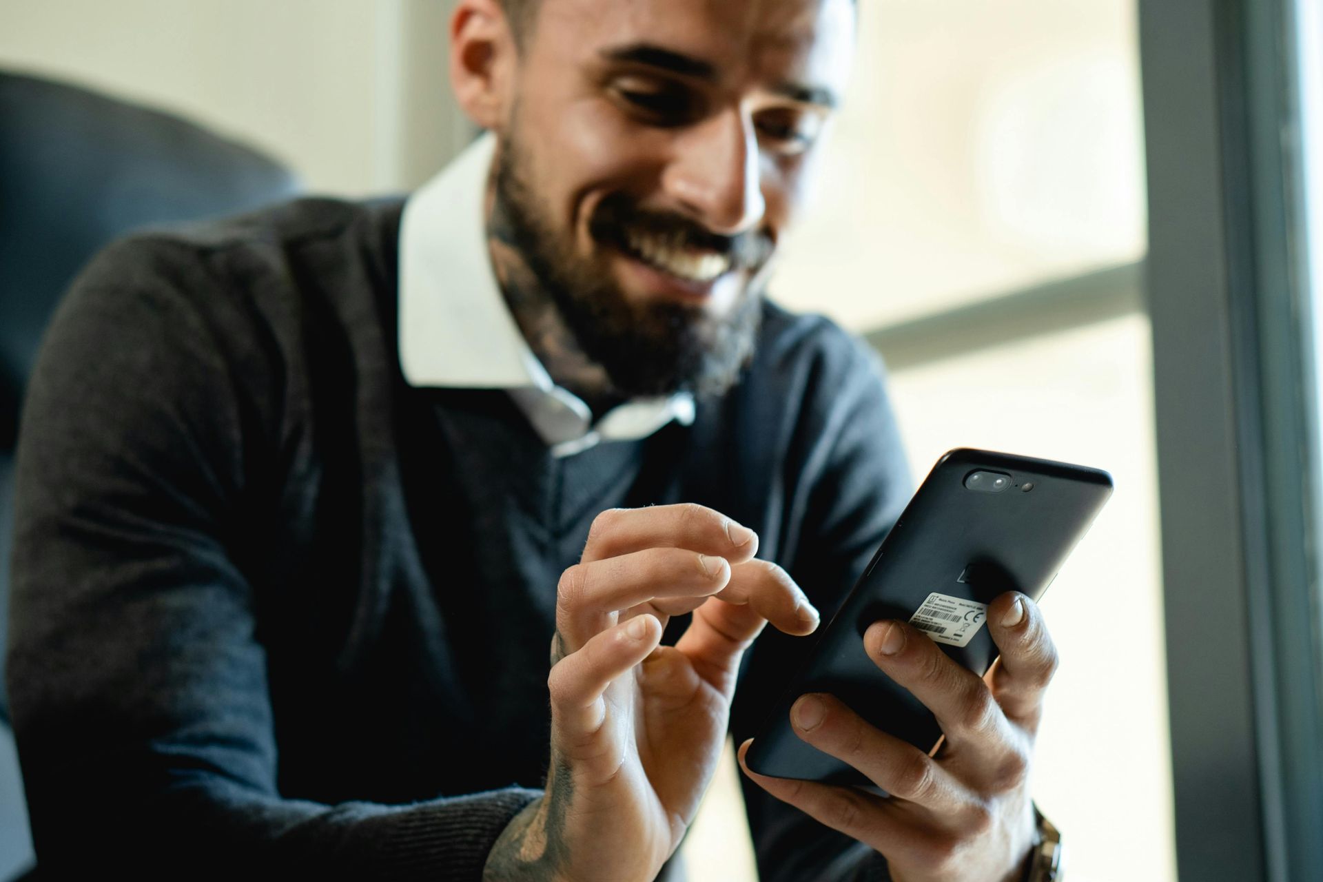 Man with beard smiles while looking at his smartphone.
