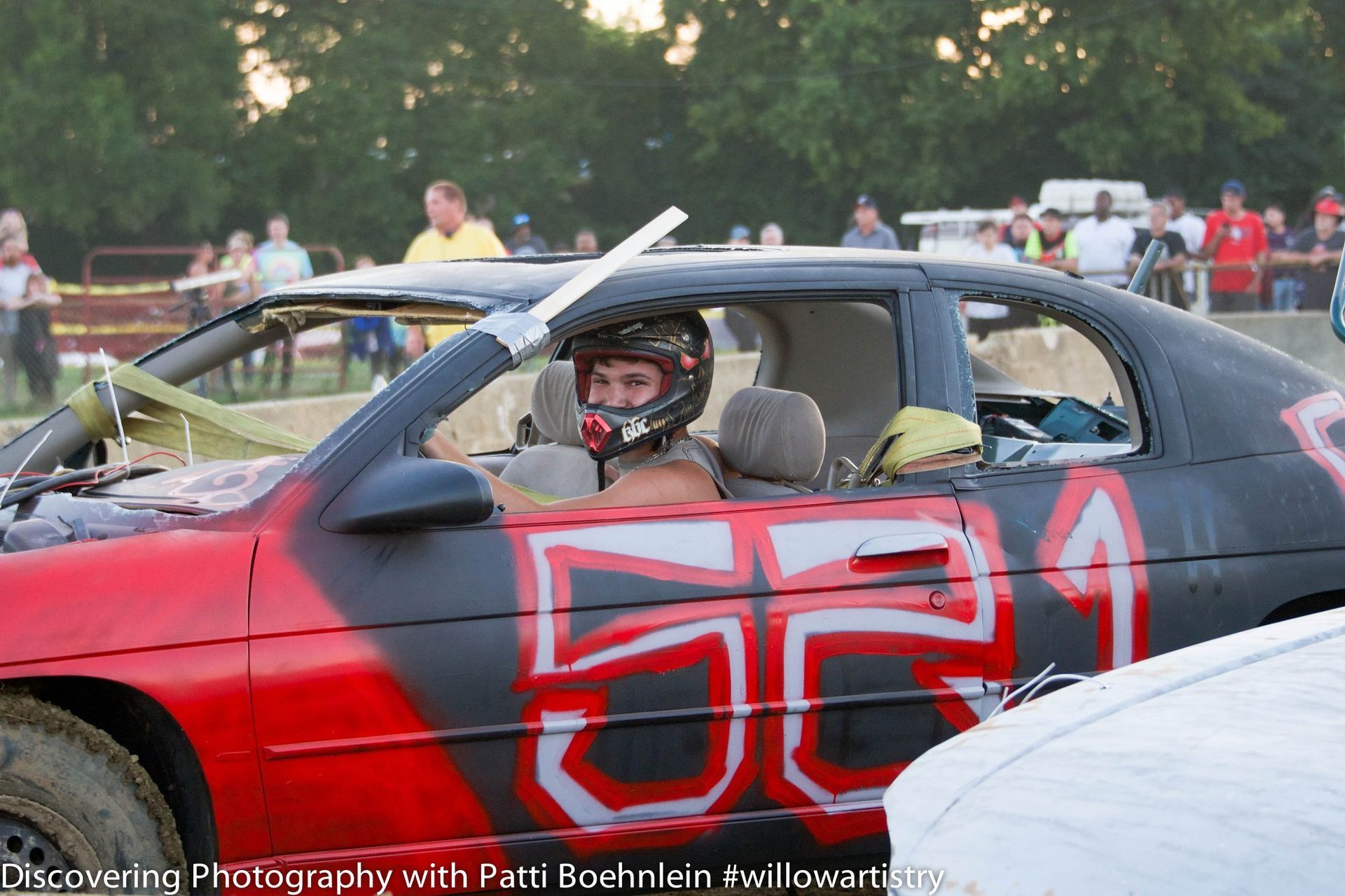 Person in a race car with number 551 on it. Red and black paint. Driver wearing a helmet.