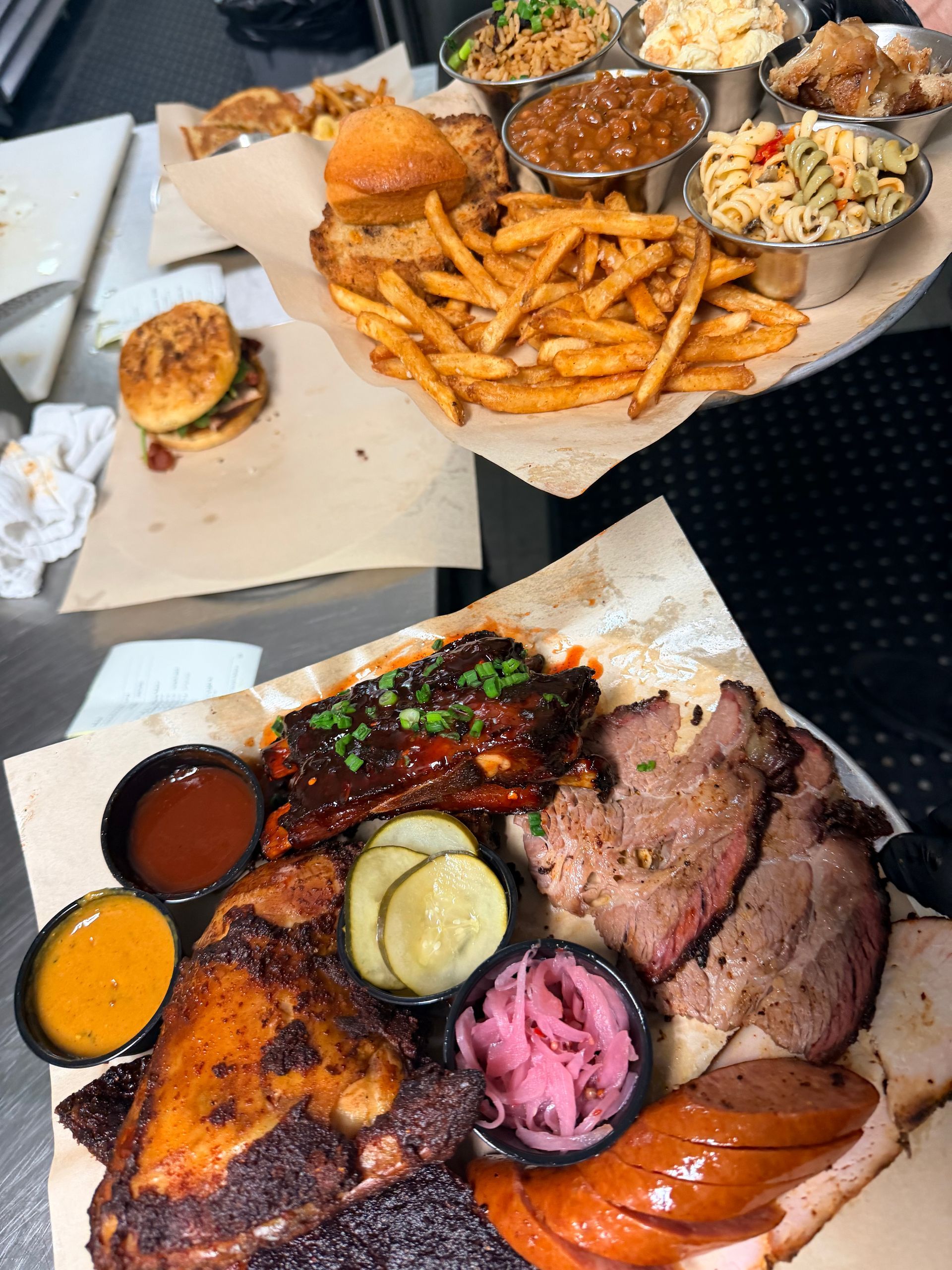Two takeout containers with barbecue meats, fries, cornbread, and coleslaw on a table.