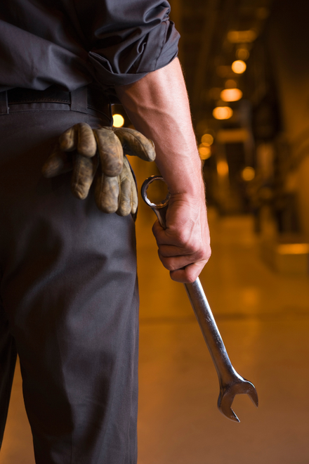 A man wearing gloves is holding a wrench behind his back.