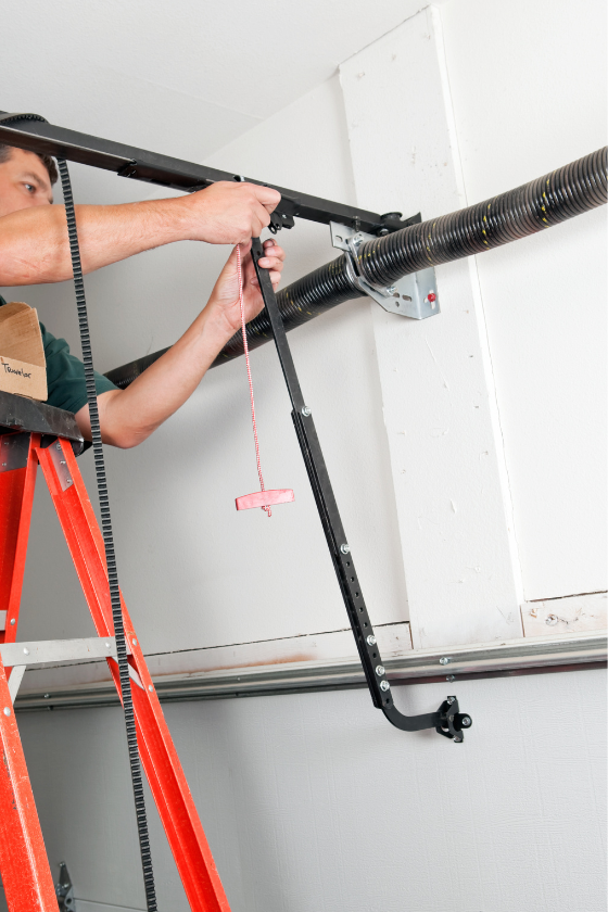 A man is standing on a ladder fixing a garage door.