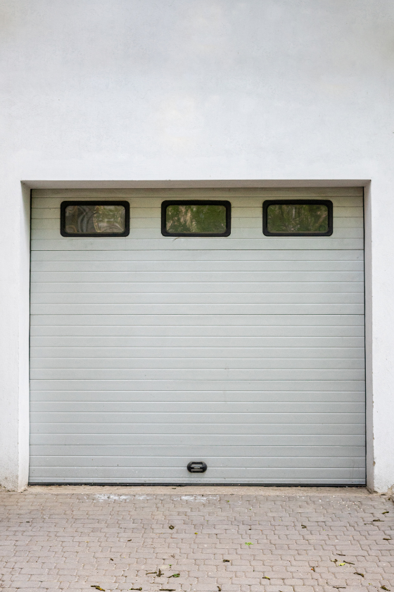A white garage door with three windows on a white wall.