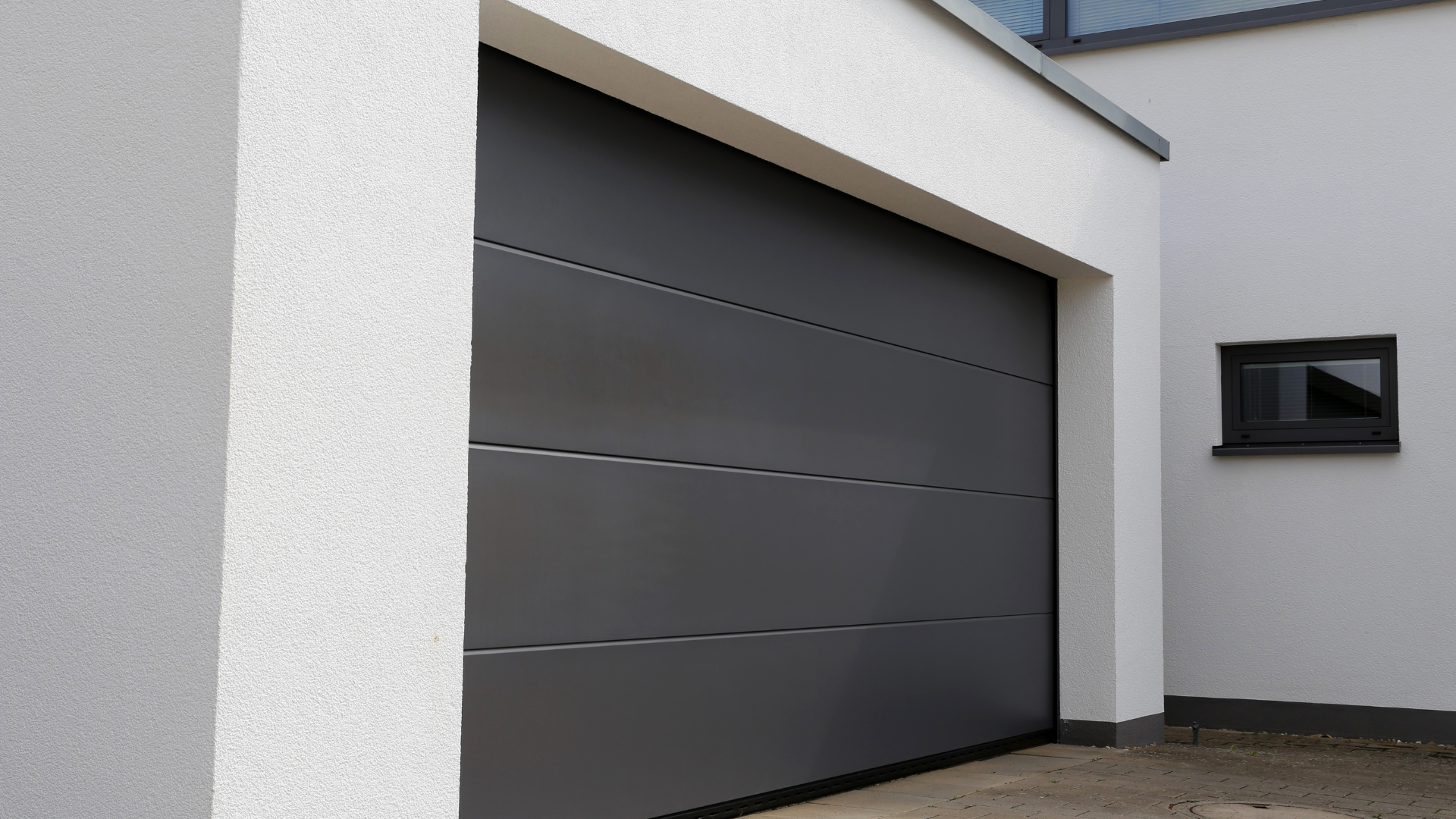 A gray garage door is sitting next to a white building.