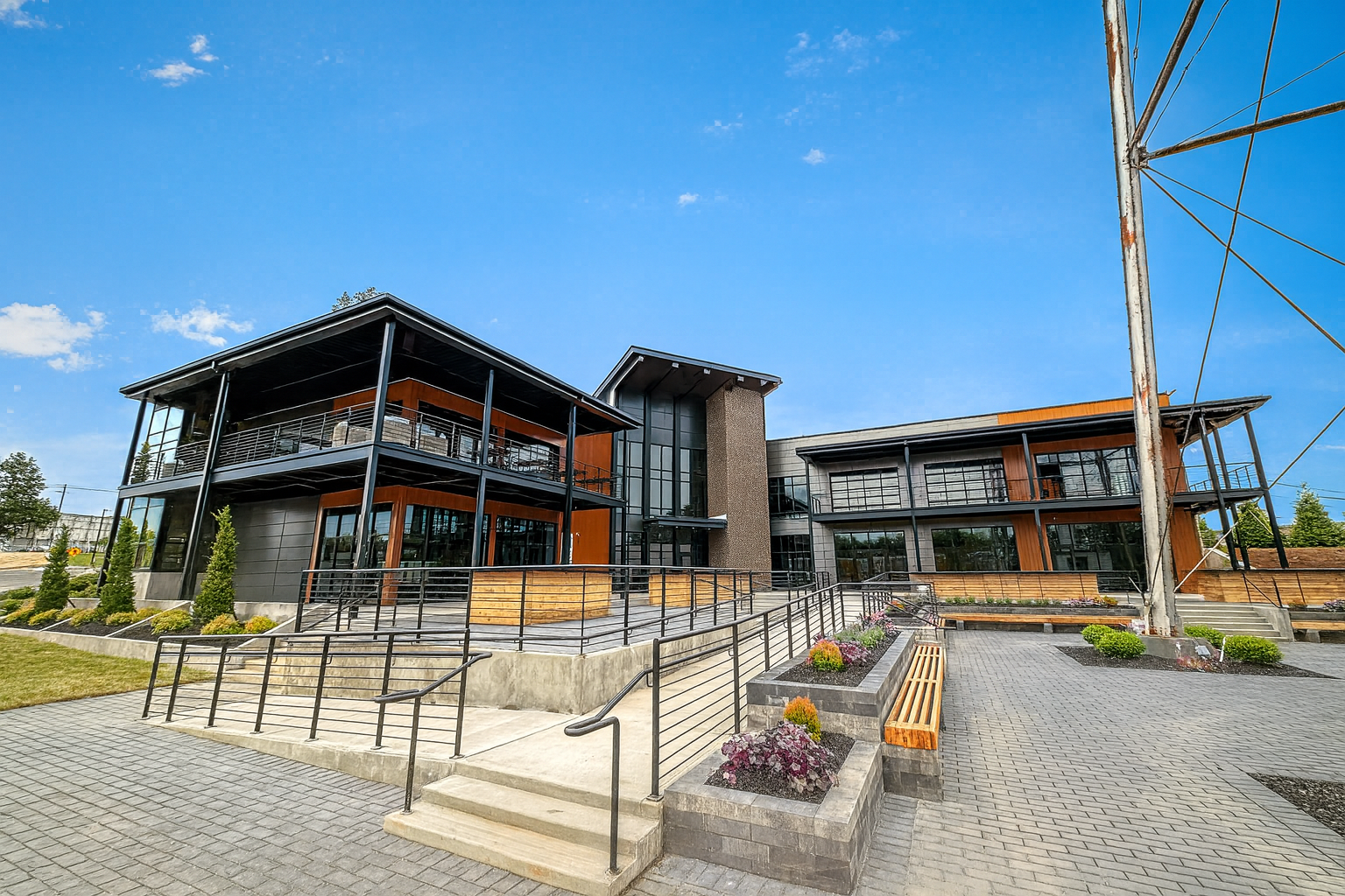 Modern two-story building with outdoor seating and cloudy sky. Stone and wooden architecture.