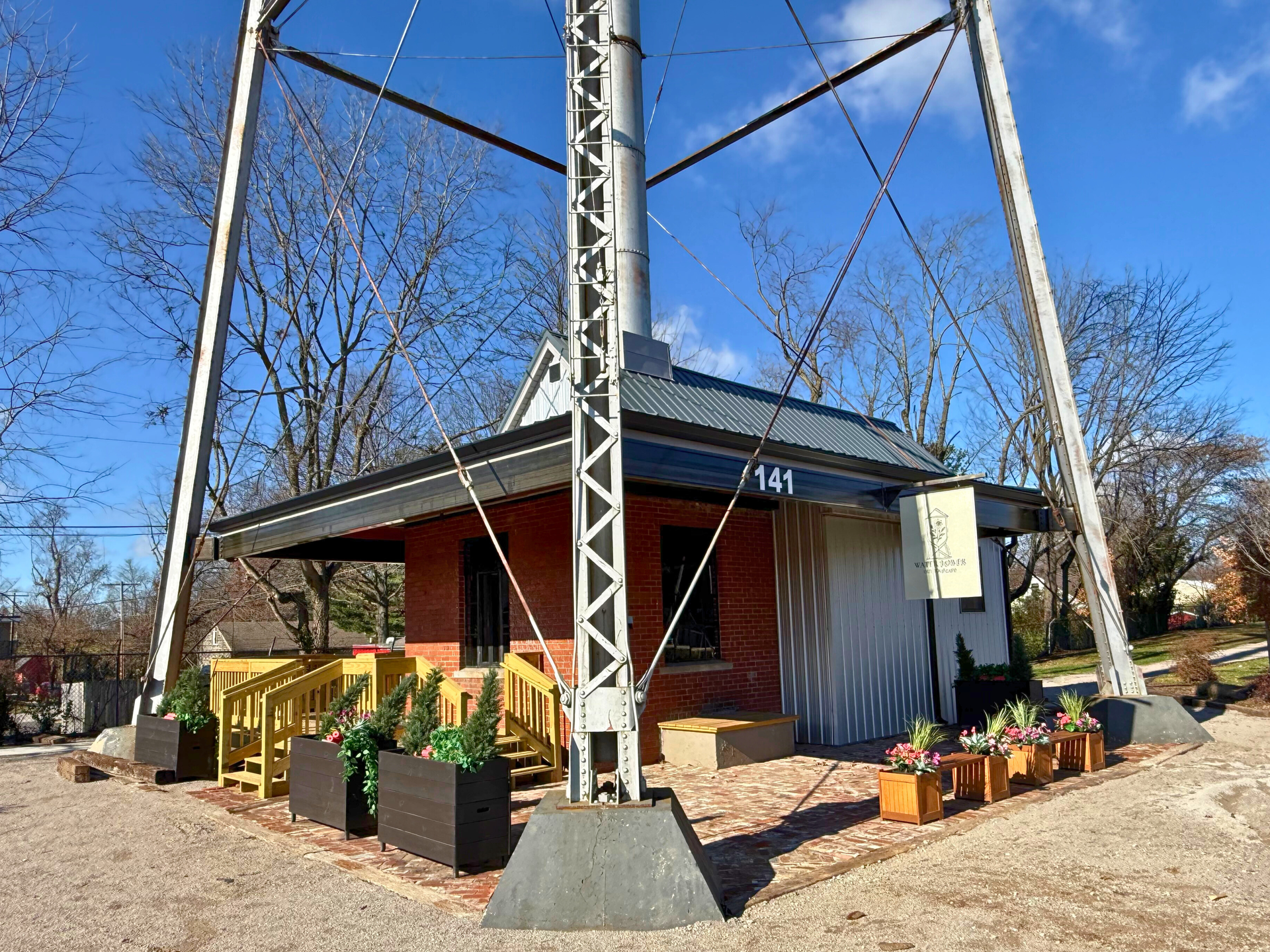 A small brick building under a metal tower; a patio with wooden planters and a sign that reads