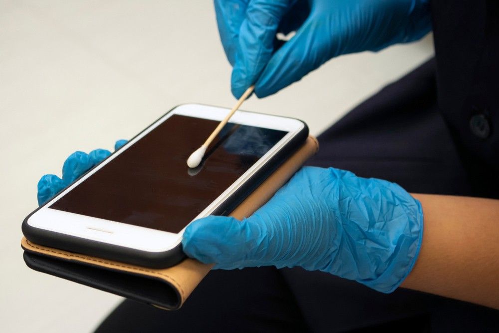 A Person Wearing Blue Gloves is Cleaning a Cell Phone — Verdi Cleaning Services in Holt, ACT