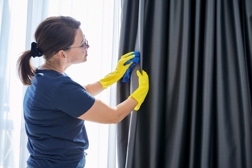 A Woman in Yellow Gloves is Cleaning a Window With a Cloth — Verdi Cleaning Services in Tuggeranong, ACT